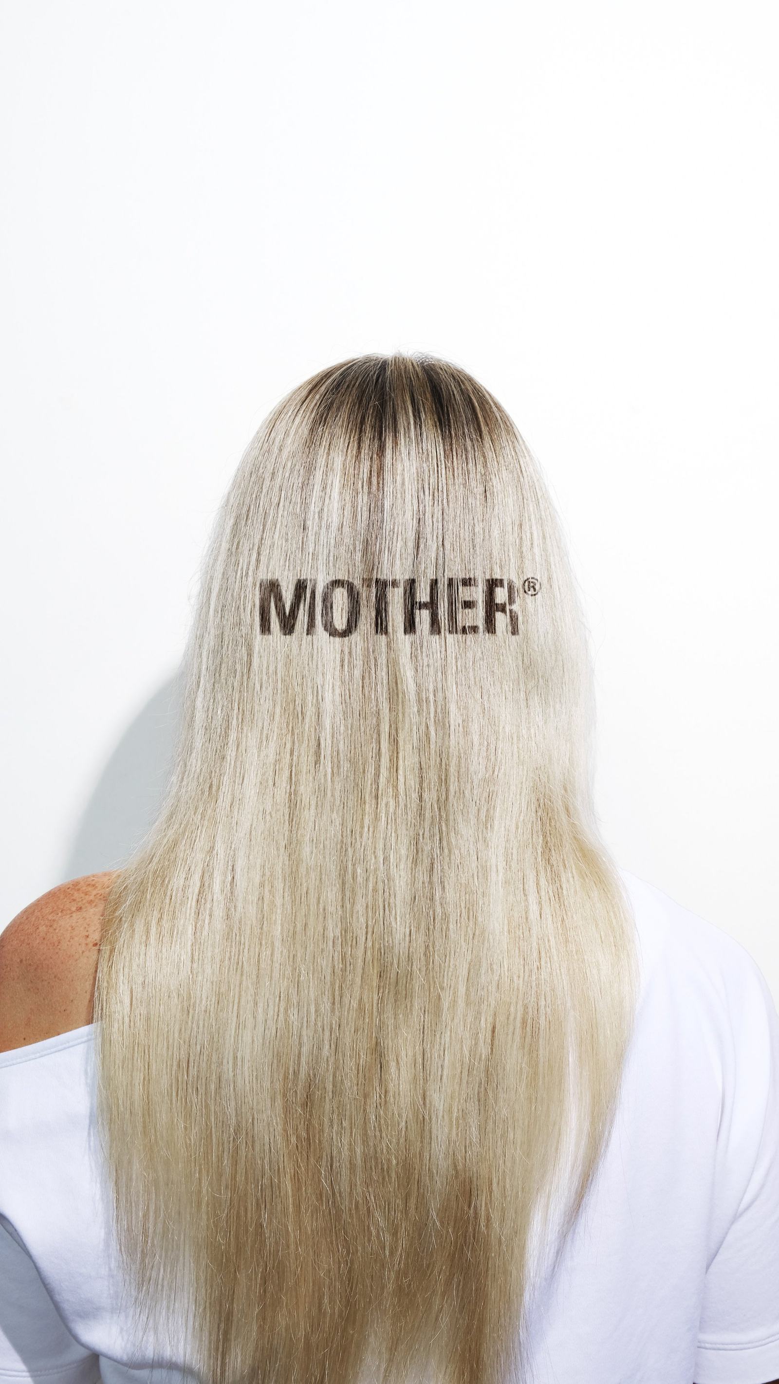 The back of a client's head, long rooted blonde with MOTHER® printed across the hair